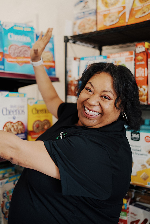 Catrina smiling in a black shirt with arms up showing off a display of cereal on a shelf