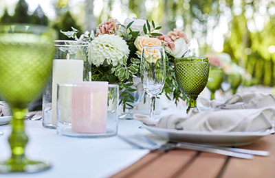 Dinner tables with white tablecloth and flowers, served with porcelain and green glasses.